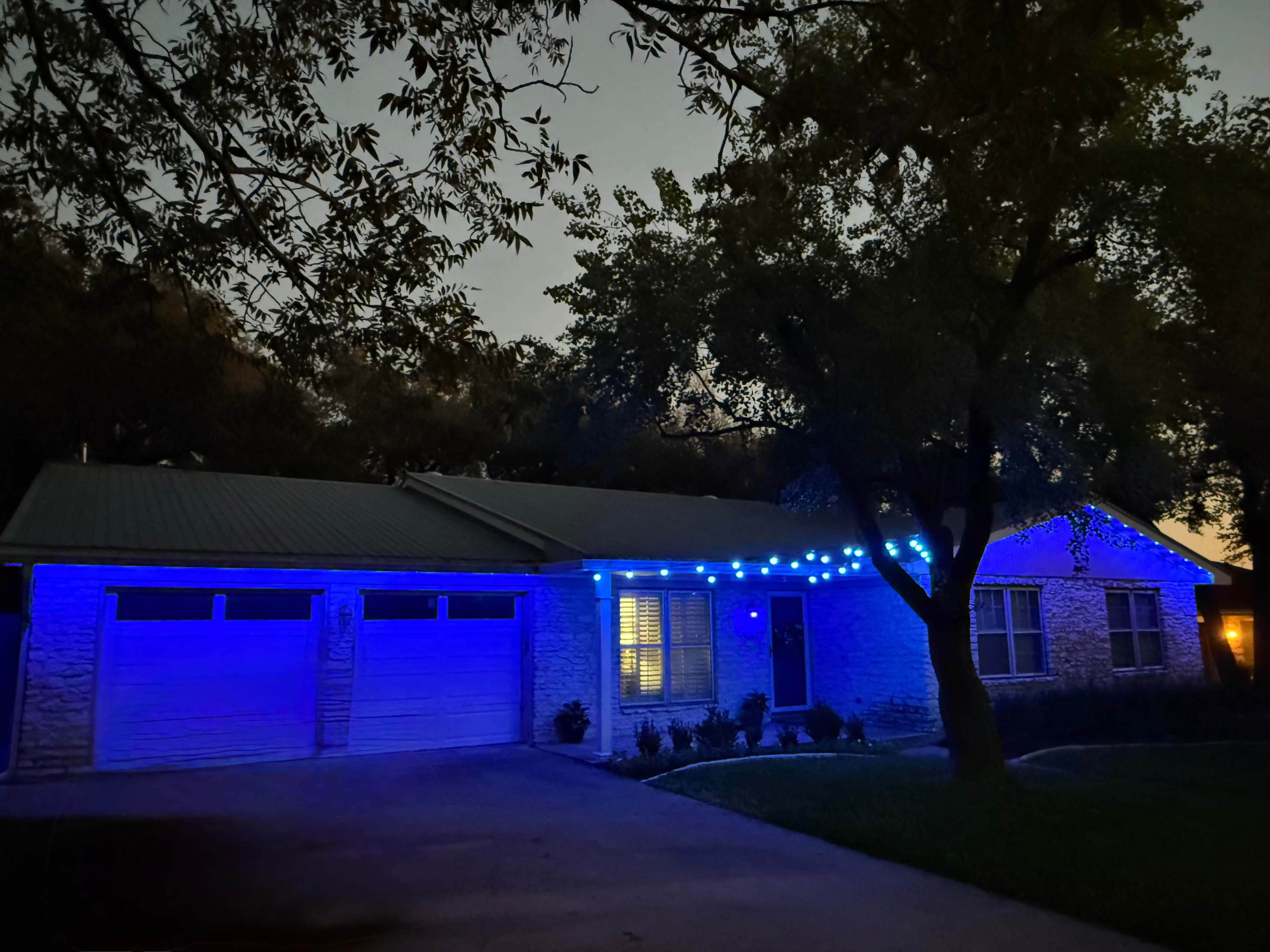 Stone house at night illuminated by bright blue string lights along the roof and garage.